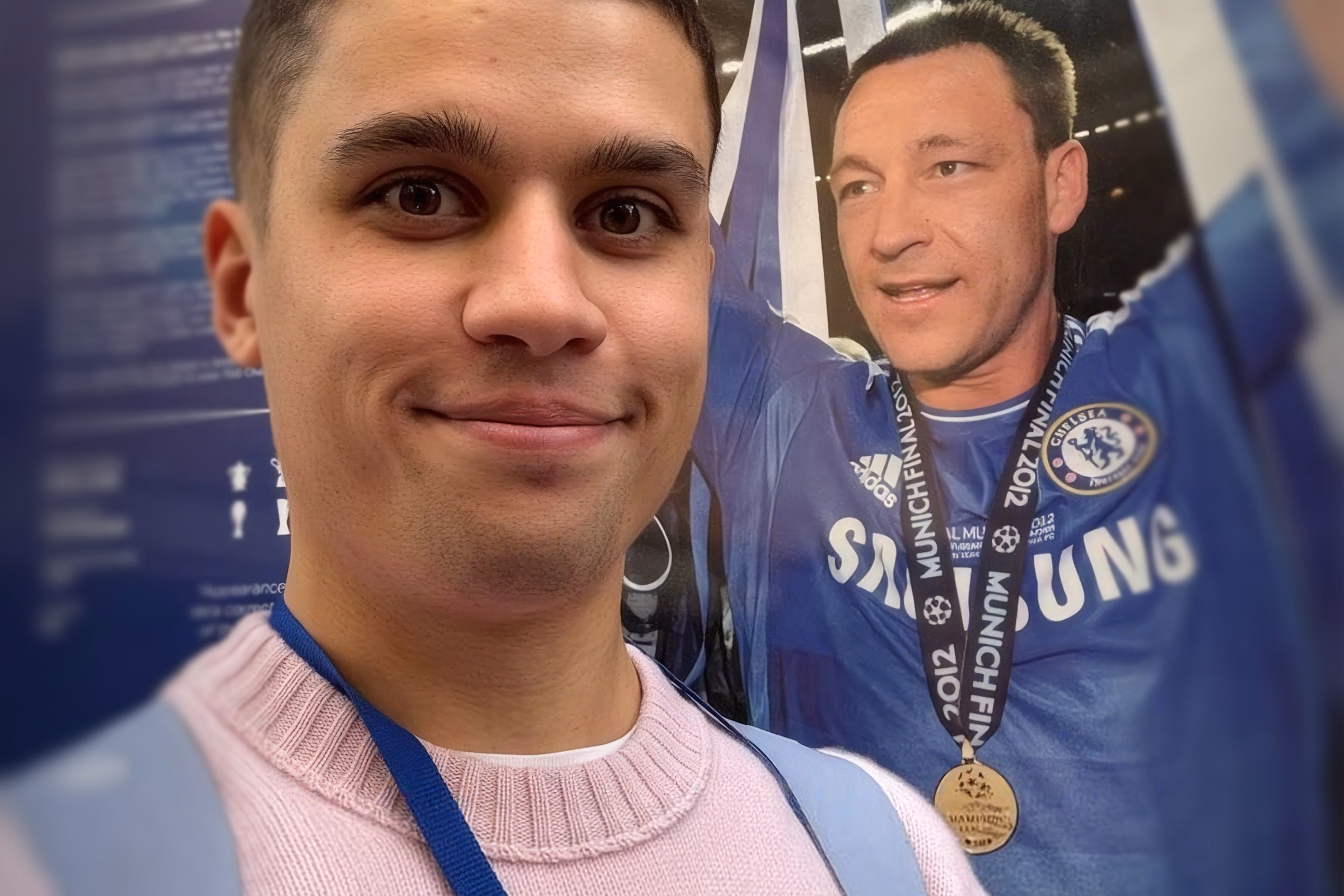 Sergey Krasotin at Chelsea FC, in front of a wall photograph of a club captain holding a Champions League medal.