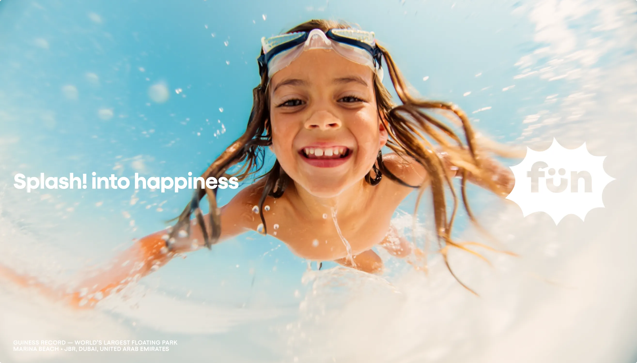 Close-up of a smiling girl in swim goggles splashing through bright blue water, with the headline Splash! into happiness and a white aqua fun starburst logo on the right