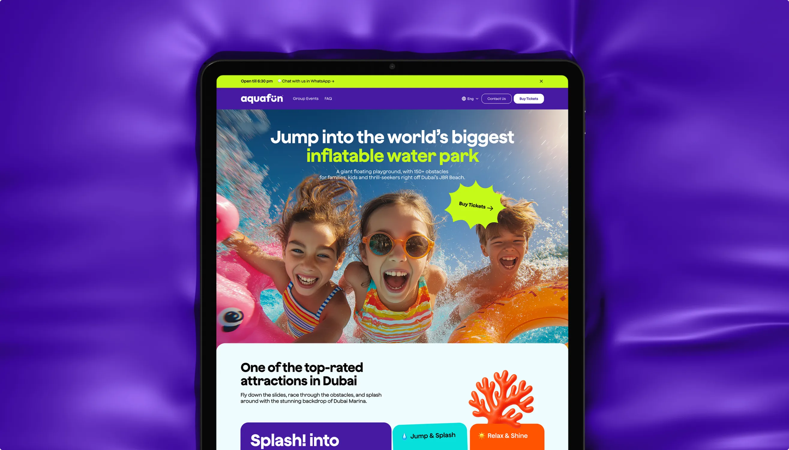 Tablet resting on a purple inflatable showing the Aquafun website hero, with cheering kids in the water and the headline Jump into the world’s biggest inflatable water park