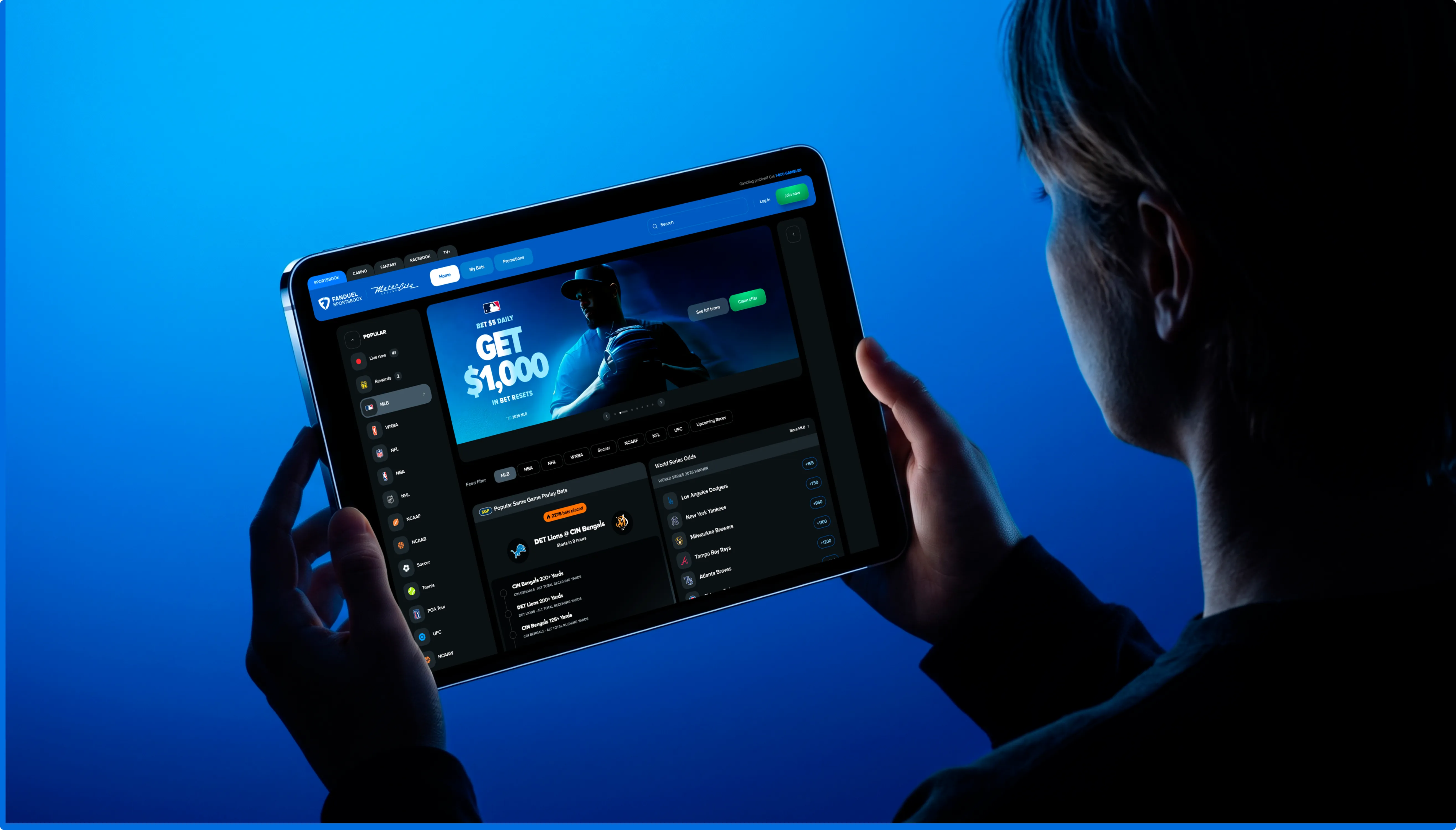 A person holding a tablet running the FanDuel app, lit in blue