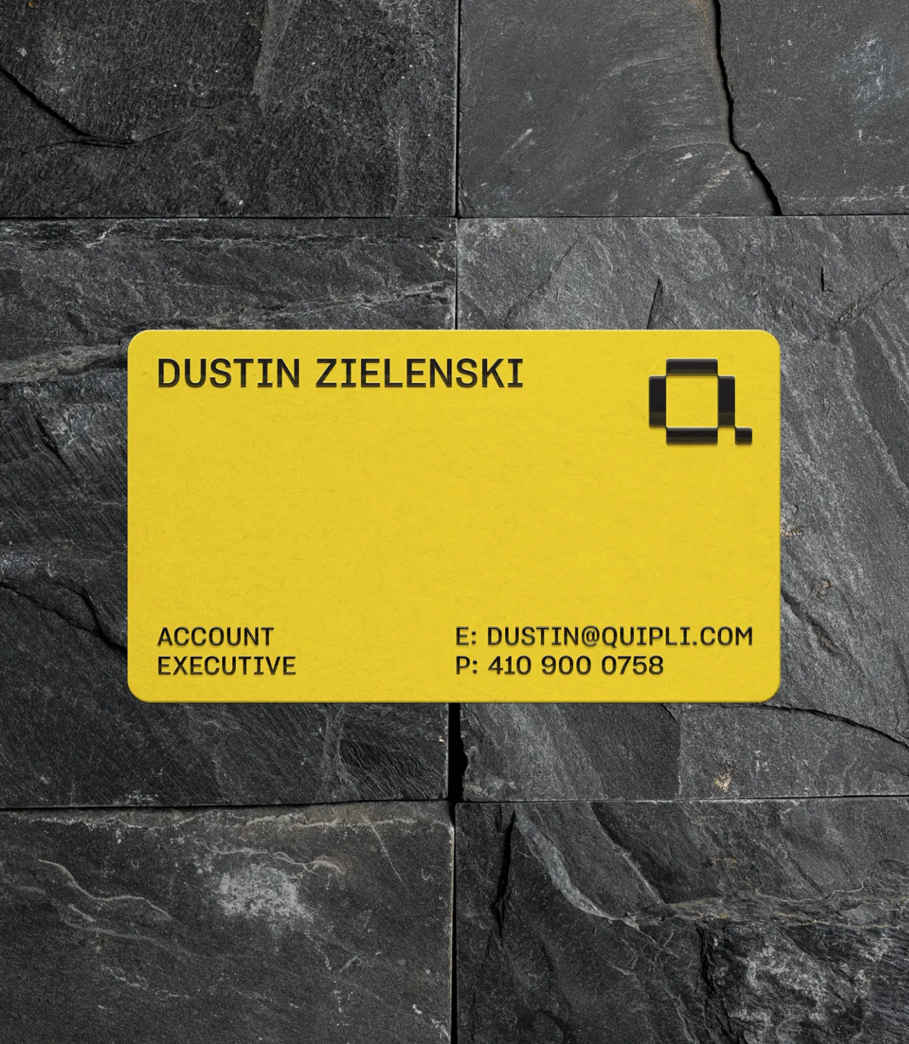 Yellow Quipli business card for an account executive resting on dark slate stone